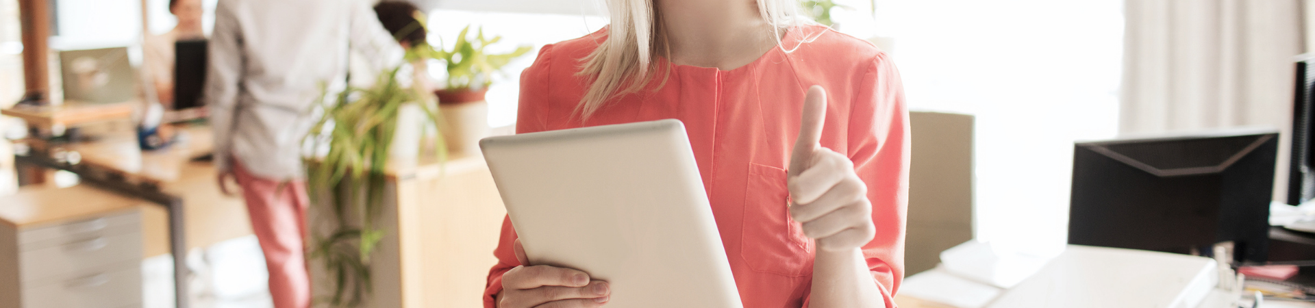 Pembe bluz giyen, bir eliyle onaylama işareti yapıp diğer eliyle tablet tutan iş kadını.